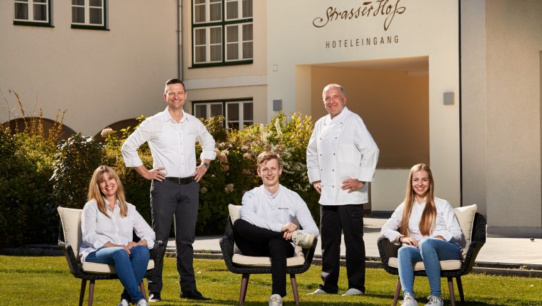Familie Eisenbock & Chefkoch Christian Schimann, © Niederösterreich Werbung/Andreas Hofer Fünf Personen posieren vor einem Gebäude mit der Aufschrift 'Eisenbock's Strasserhof Hoteleingang'.