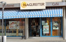Bäckerei&Konditorei Naglreiter Fischamend, © Donau Niederösterreich Birgit Köck Eingang einer Bäckerei mit blau-weiß gestreifter Markise und Schildern für Angebote.