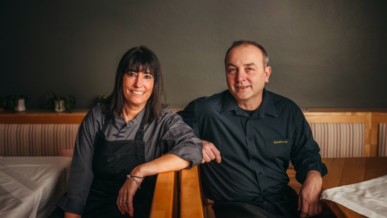 Wirtsleute Barbara und Manuel Langer, © Niederösterreich Werbung/Daniela Führer Zwei Personen in Arbeitskleidung sitzen lächelnd in einem Restaurant.