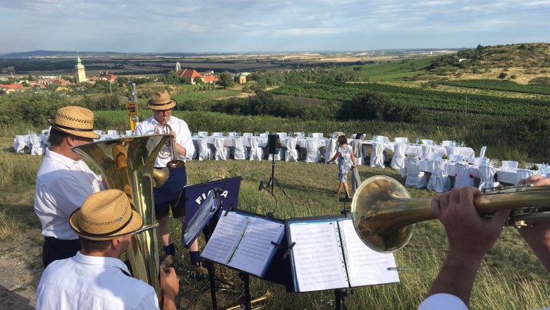 Tafeln im Weinviertel, © Weinviertel Tourismus GmbH Blasmusikgruppe spielt im Freien vor gedeckten Tischen und Weinbergen.