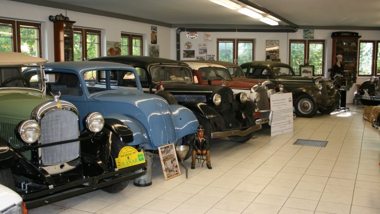 Oldtimermuseum Hausberger, © Leonhard Hausberger Innenansicht eines Oldtimermuseums mit mehreren klassischen Autos in einer Reihe.