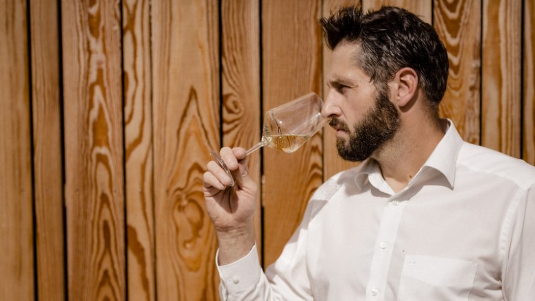 Das Verkosten der Weine ist auch ein wichtiger Teil der Winzerarbeit, © Astrid Bartl Mann riecht an einem Weinglas vor Holzwand.