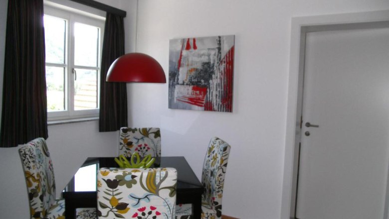 Landhaus Rossatz, © Familie Schlager Essbereich mit floral gemusterten Stühlen, roter Hängelampe und modernem Kunstwerk an der Wand.