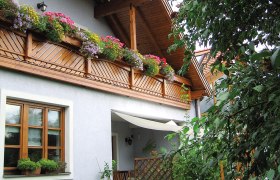 Gästehaus Helma Klinglhuber, © Klinglhuber Ein Gästehaus mit Holzbalkon und blühenden Blumen, umgeben von grünen Pflanzen.
