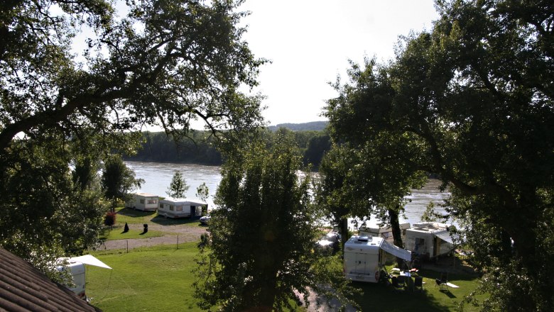 Campingplatz, © Szilágyi Campingplatz am Fluss mit Wohnwagen und Bäumen.