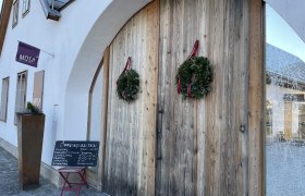 Cafe-Bar Mosa, © Wiener Alpen/Katharina Lechner Eingang der Cafe-Bar Mosa mit Holztür und Kränzen.