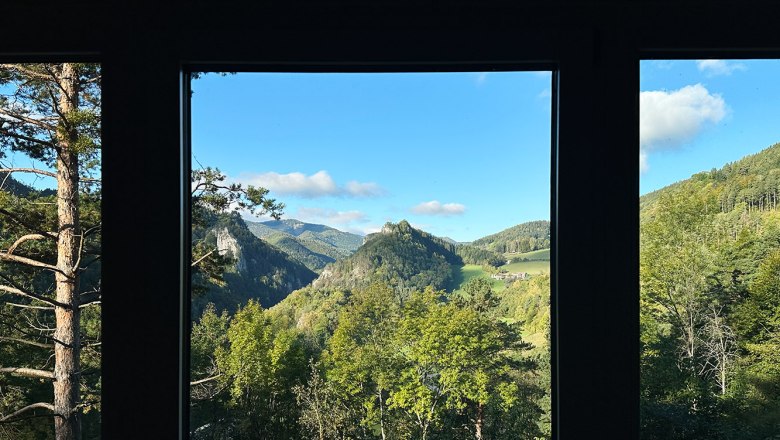Aussicht, © Meinrad Hofer Blick aus einem Fenster auf eine grüne Berglandschaft mit blauem Himmel.