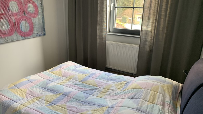 Schlafzimmer, © Fam. Wochesländer Schlafzimmer mit Bett, bunter Decke, Fenster und Kunstwerk an der Wand.
