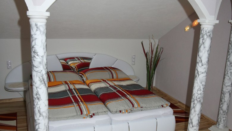 Wohlfühlen im Holzhackerdorf Karlstift, © Manfred Gill Schlafzimmer mit Doppelbett, Marmorsäulen und gestreifter Bettwäsche.