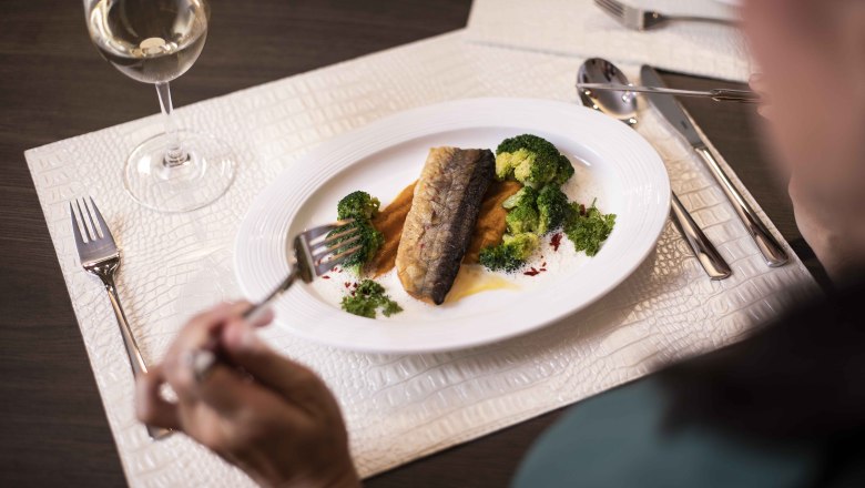 Dinner, © NMC Ein Teller mit Fischfilet, Brokkoli und Soße, daneben ein Glas Weißwein.