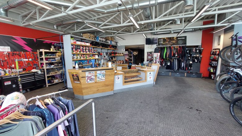 Bikestore.cc, © Bikestore.cc Innenansicht eines Fahrradgeschäfts mit Werkstattbereich, Verkaufstresen und Fahrradzubehör.