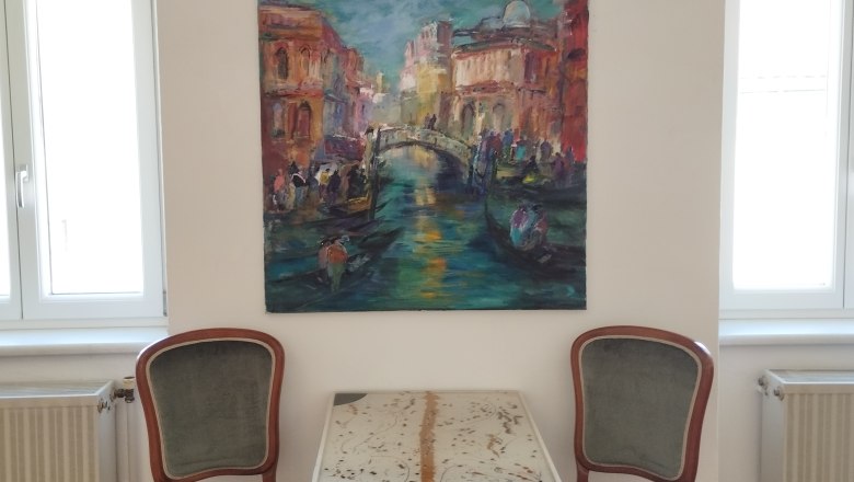 die Galerie MERKIMA, © Doris Hauser Zwei Stühle und ein Tisch vor einem Gemälde an einer weißen Wand.