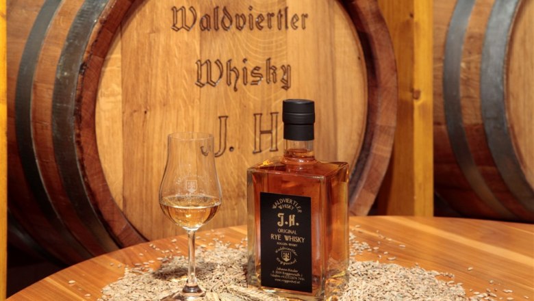 Whisky-Erlebniswelt Haider, © Whisky-Erlebniswelt Haider Flasche Waldviertler Whisky und Glas auf Tisch mit Getreide vor Holzfass.