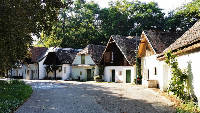 Peigarten Peregriniplatzl, © Weinstraße Weinviertel Eine malerische Gasse mit traditionellen weißen Häusern und schrägen Dächern, umgeben von Bäumen.