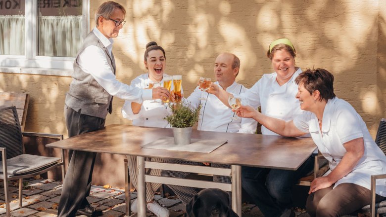 Starkes Wirtshaus-Team, © Niederösterreich Werbung/Daniela Führer Ein Team von fünf Personen stößt draußen an einem Tisch an, mit einem schwarzen Hund im Vordergrund.