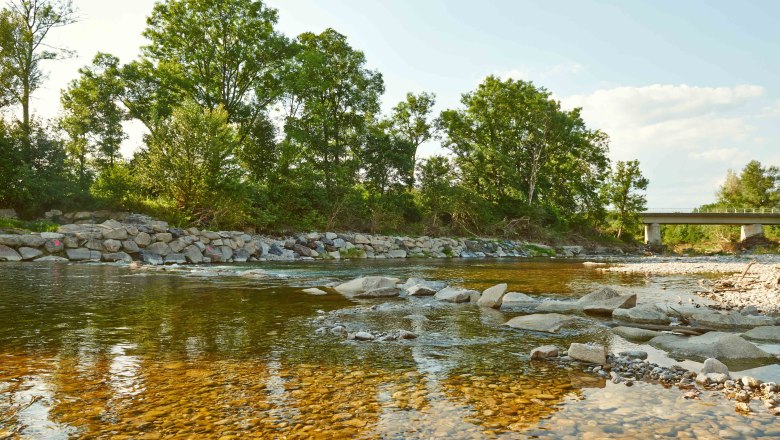 Natur in Erlauf, © Klaus Engelmayer Fluss mit klarem Wasser, umgeben von Bäumen und einer Brücke im Hintergrund.