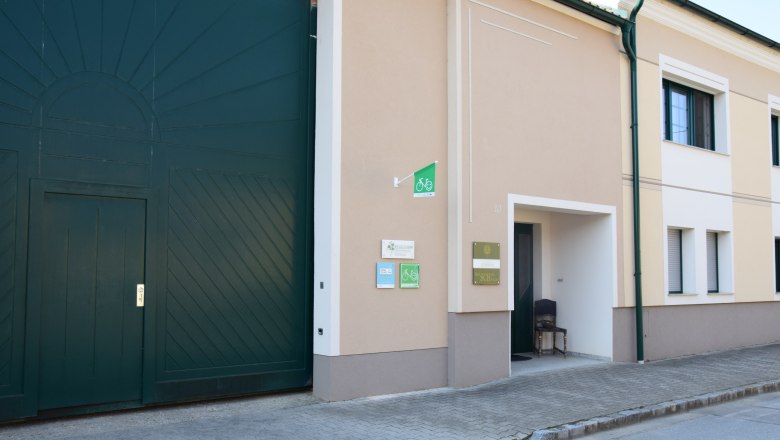 Weingut, © Familie Schwalm Eingang eines Weinguts mit großen grünen Toren und Schildern an der Wand.