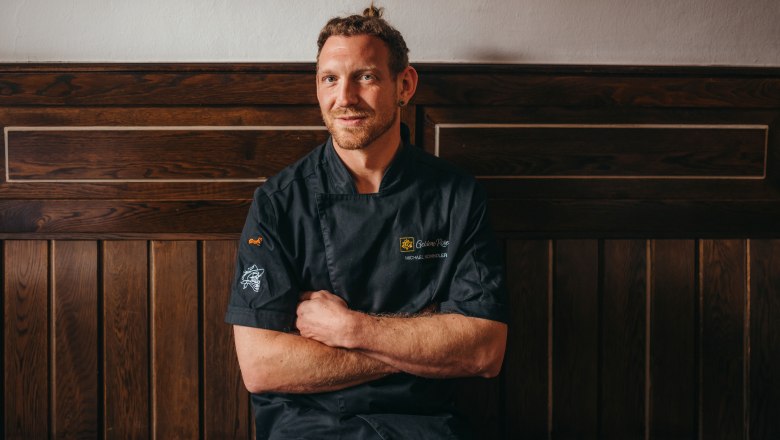 Wirt Michael Schindler, © Niederösterreich Werbung/Daniela Führer Ein Mann in schwarzer Kochjacke sitzt vor einer Holzwand.