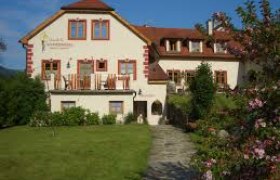 Haus Schneeweiss, © Birgit Schneeweiss Ein großes, traditionelles Haus mit rotem Dach und blühendem Garten im Vordergrund.