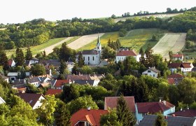 Kirche Hl. Leonhard, © Gemeinde Kreuttal Landschaft mit Kirche und Dorf im Vordergrund, umgeben von Feldern und Hügeln.