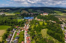 Haus Morgensonne-Region, © Fam. Pauker Luftaufnahme einer ländlichen Region mit Feldern, einem See und einem Schloss auf einem Hügel.