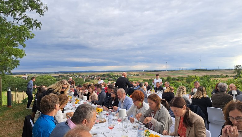 Tafeln im Weinviertel, © Weinviertel Tourismus GmbH Menschen sitzen an langen Tischen im Freien mit Blick auf eine ländliche Landschaft.