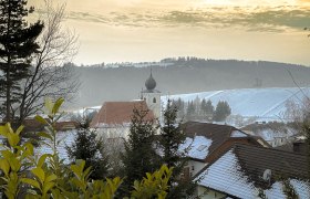 Gemeinde Hollenthon, © Gabi Grill Winterliche Landschaft in Hollenthon mit schneebedeckten Dächern und einer Kirche im Hintergrund.