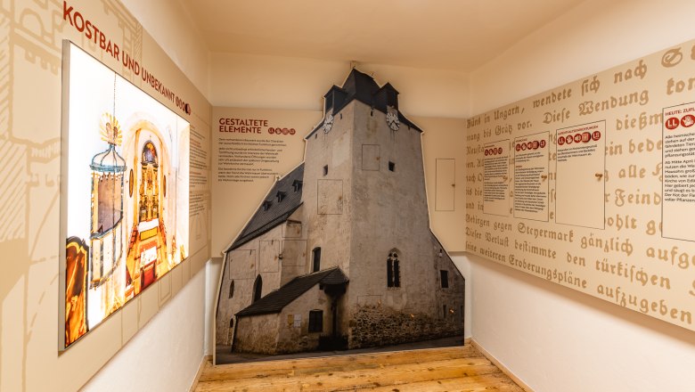Wehrkirchendokumentation, © Wiener Alpen, Christian Kremsl Innenansicht einer Ausstellung über Wehrkirchen mit Texttafeln und einem raumhohen Bild einer Kirche.