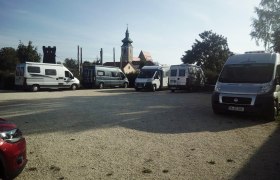 Wohnmobilstellplatz, © Sportunion Pillichsdorf Wohnmobilstellplatz mit mehreren geparkten Wohnmobilen und einer Kirche im Hintergrund.