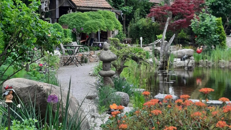 GrünTon Cottage Kralovec, © GrünTon Cottage Kralovec Ein idyllischer Garten mit Teich, bunten Blumen und einem kleinen Cottage im Hintergrund.