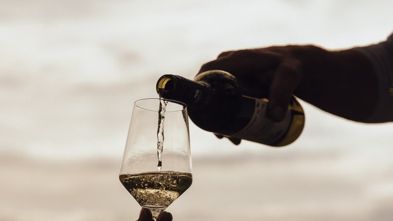 Wein einschenken, © Weinviertel Tourismus / Sophie Menegaldo Wein wird in ein Glas im Freien eingeschenkt, im Hintergrund eine Landschaft.