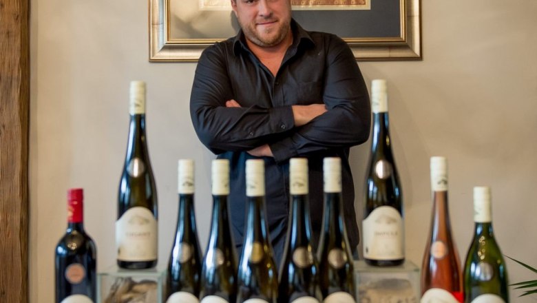 Toni Zöhrer, © Weingut Zöhrer Mann steht hinter einer Reihe von Weinflaschen auf einem Tisch.
