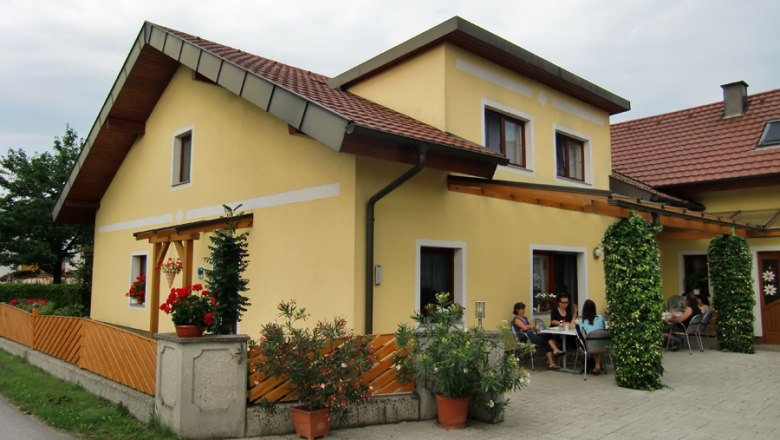 Ferienwohnungen & Privatzimmer Leeb, © Privatzimmer Leeb Gelbes Haus mit Terrasse und Menschen, die draußen sitzen.