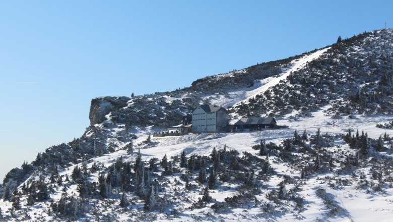 Ottohaus im Winter, © Scharfegger´s Raxalpen Resort Winterlandschaft mit dem Ottohaus auf einem verschneiten Berg unter klarem Himmel.