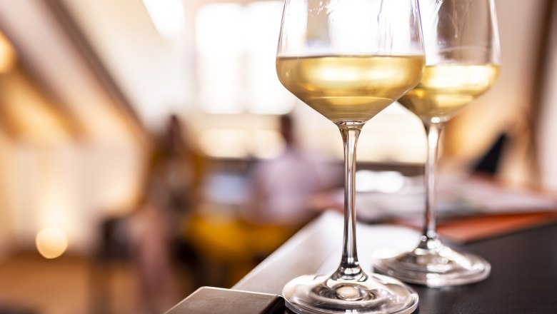 Den Wein genießen, © Weinviertel Tourismus GmbH / Herbst Zwei Gläser Weißwein auf einem Tisch, unscharfer Hintergrund.