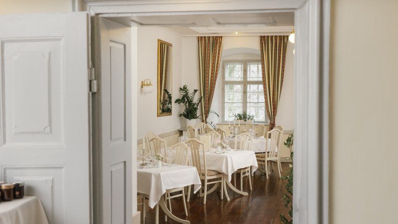 Schlossrestaurant Gloggnitz, © Wiener Alpen/ Sophie Menegaldo Elegantes Restaurant mit gedeckten Tischen, weißen Tischdecken und klassischen Stühlen, durch eine geöffnete Tür sichtbar.
