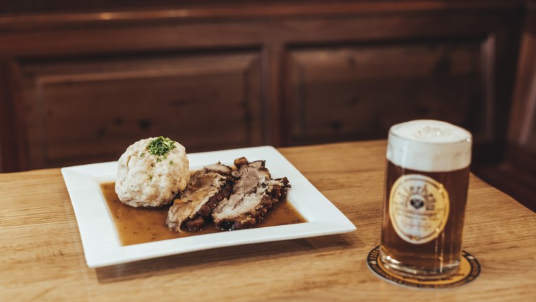 Klassische Wirtshausküche, © Niederösterreich Werbung/David Schreiber Ein Teller mit Schweinebraten und Knödel neben einem Glas Bier auf einem Holztisch.