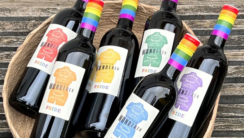 Einmalig und BIO - Pride Weine, © Stefan Jurecek Sechs Weinflaschen mit Regenbogenetiketten in einem Korb auf Holztisch.