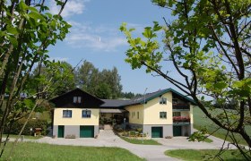 Ferienhaus, © Pölzl Ein großes gelbes Ferienhaus mit grünen Garagentoren, umgeben von Bäumen und Wiesen.