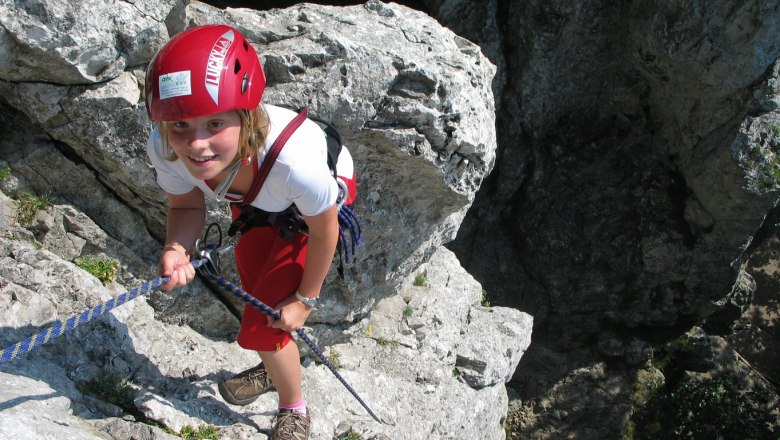 Alpinschule Peilstein, © Alpinschule Peilstein Person klettert an Felsen mit rotem Helm und Seil.