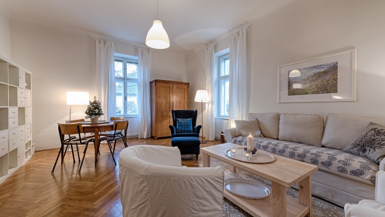 Top 1 - Wohnzimmer, © VP FeWo OG Gemütliches Wohnzimmer mit Sofa, Sessel, Esstisch und Regalen.