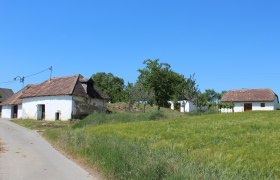 Roseldorfer Kellergasse, © Weinviertel Tourismus Ländliche Szene mit alten Gebäuden und grünen Feldern unter blauem Himmel.