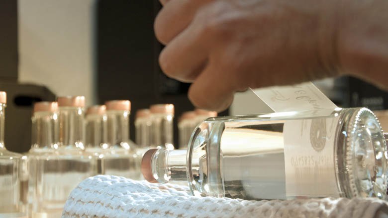 Edelbrände der Familie Hauser, © Reinhard Srb Nahaufnahme einer Hand, die ein Etikett auf eine Flasche Edelbrand klebt.