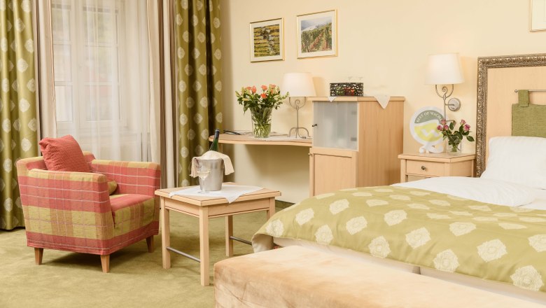 Details im Zimmer vom Hotel-Restaurant Zur Post, © BOW Rita Newman Gemütliches Hotelzimmer mit grünem Teppich, rotem Sessel, Tisch mit Sektkühler, Blumen und Bett mit grünem Überwurf.