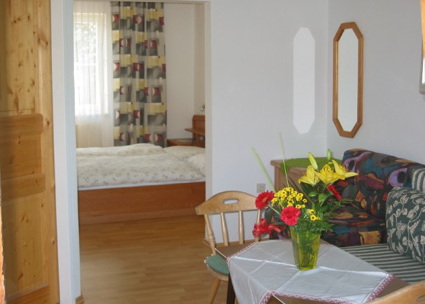 Ottensteinerhof-Waldblick, © Ottensteinerhof-Waldblick Wohnzimmer mit Tisch, Blumenstrauß und Blick ins Schlafzimmer.