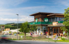 Eis-Greissler Welt, © Blochberger Eisproduktion GmbH Gebäude der Eis-Greissler Welt mit Bäumen und Besuchern und Blick auf den Erlebnispark.