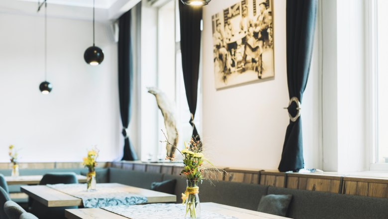 Im Herzen von Berndorf, © Niederösterreich Werbung/David Schreiber Innenansicht eines stilvollen Cafés mit Holztischen, Blumenvasen und schwarzen Vorhängen.