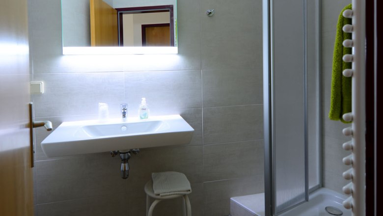 Badezimmer im Gasthof Schmied Smolka, © Gasthof Schmied Smolka Modernes Badezimmer mit Waschbecken, beleuchteter Spiegel und Dusche.