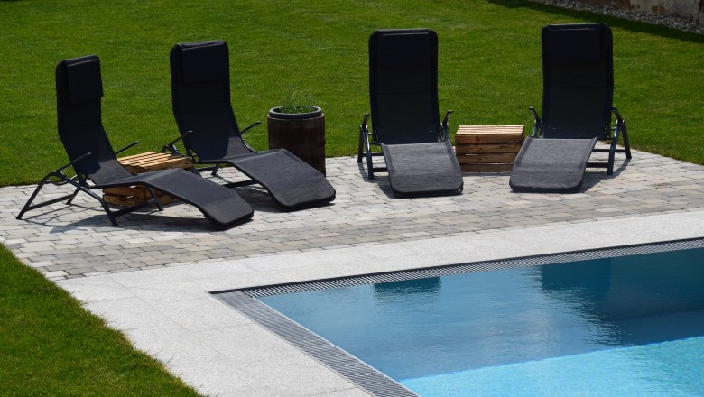 Gästebereich im Garten am Pool, © Familie Schwalm Vier schwarze Liegestühle am Pool auf einer gepflasterten Fläche im Garten.