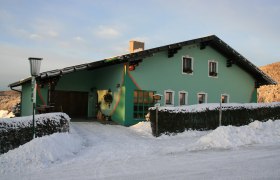 Winteransicht Privatzpension Karl Buchner, © Karl Buchner Grünes Haus im Schnee mit dekorativen Elementen und Laterne.
